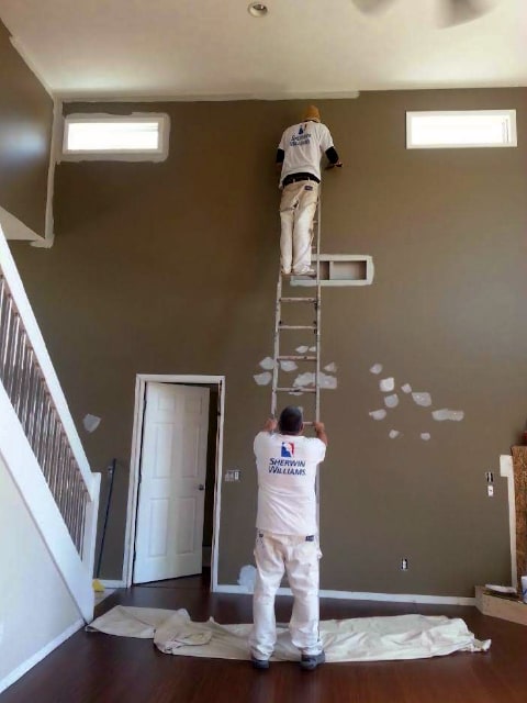 2 painters using a ladder to paint a high wall
