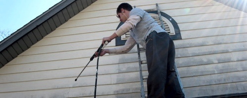 A person on a ladder power washing siding